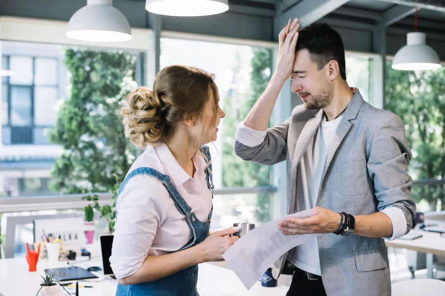 man slapping forehead beside woman, in an office setting