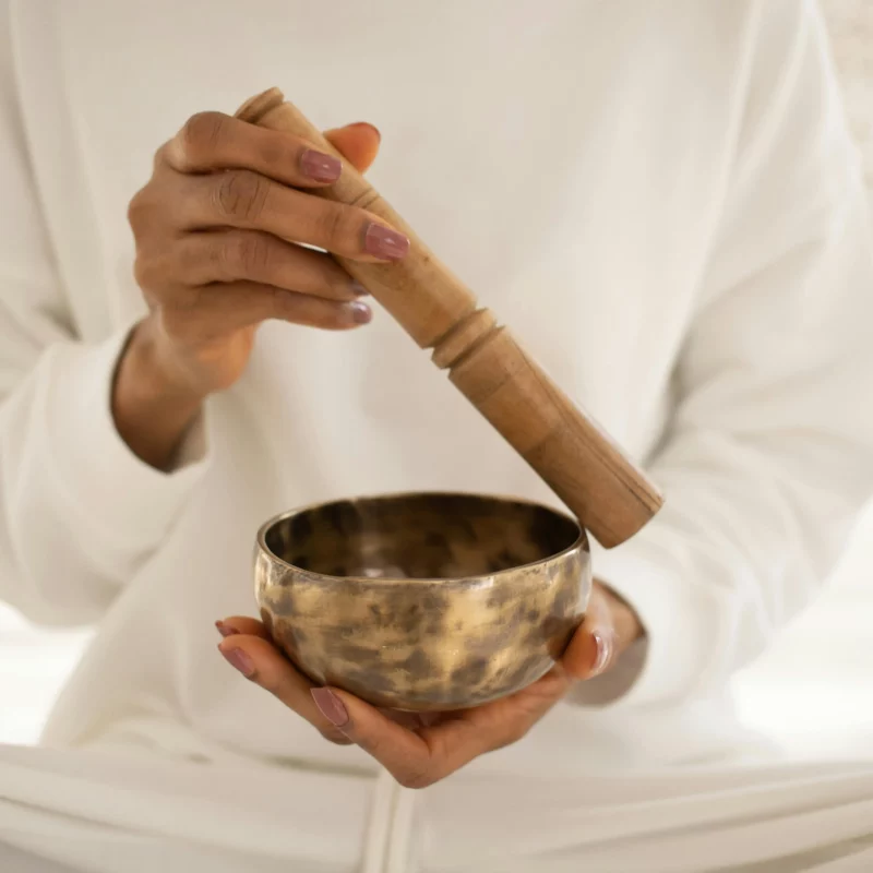 Image of a woman wearing all white holding a Tibetan singing bowl